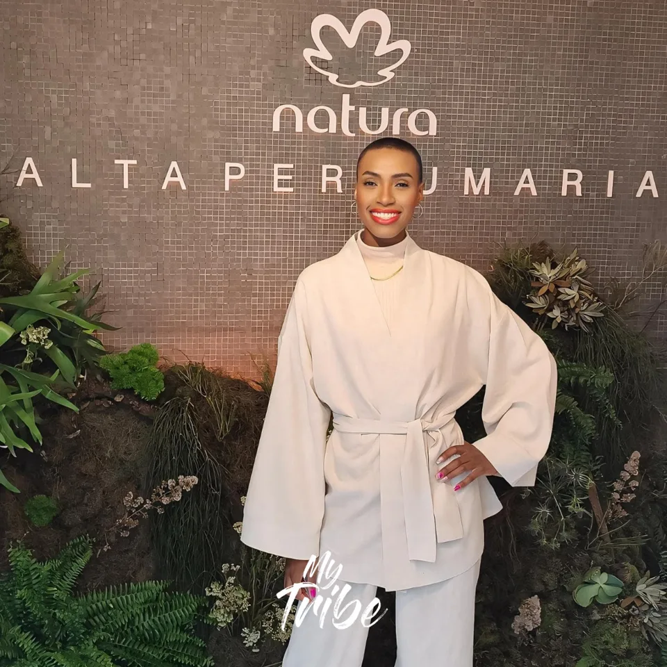 Modelo sorrindo de conjunto claro no painel da Natura Alta Perfumaria em evento de lançamento