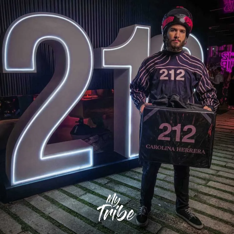 Profissional caracterizado de motoboy com bag da 212 Carolina Herrera em evento de lançamento