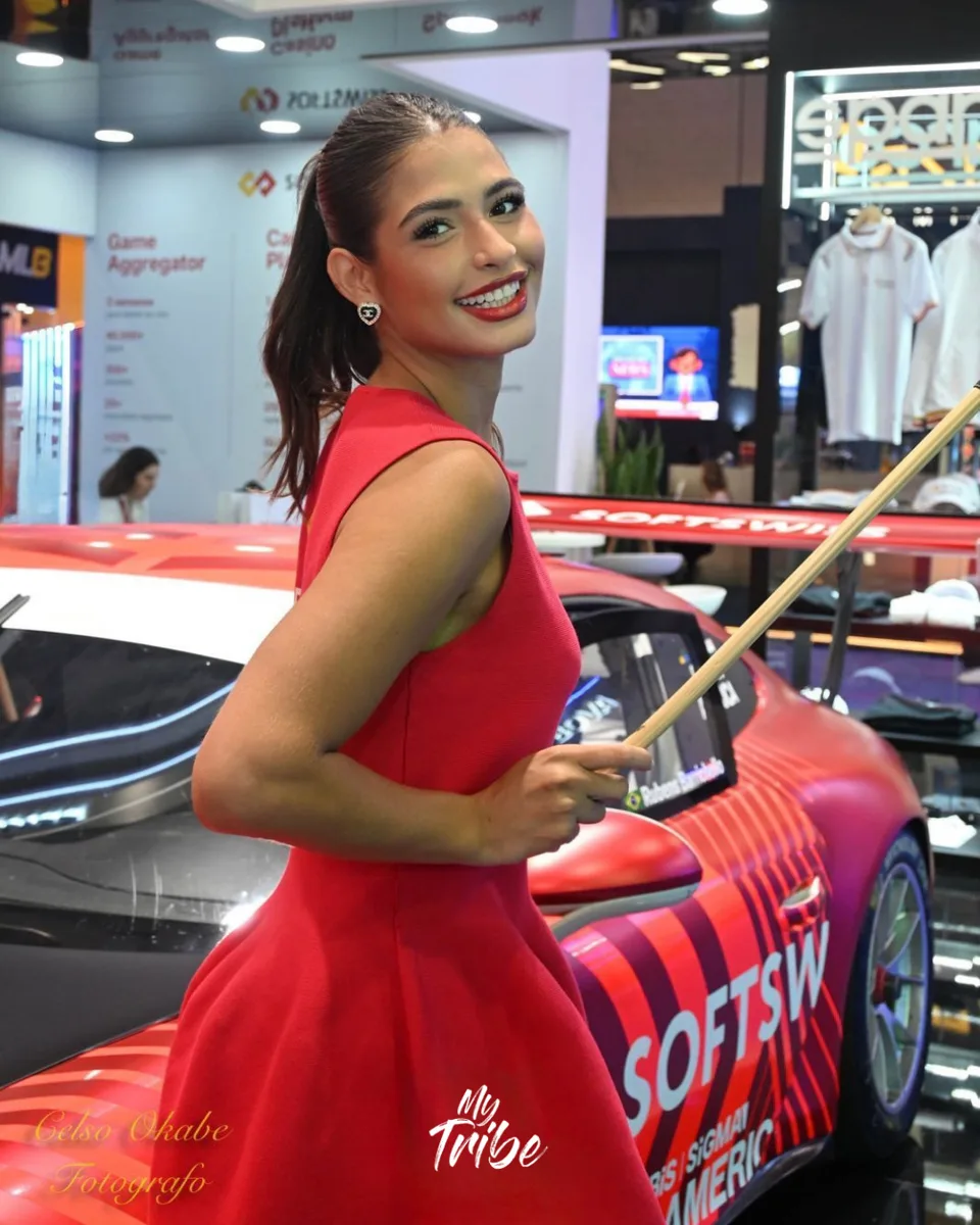 Promotora de vestido vermelho apresentando o carro de corrida no estande da Softswiss em feira internacional