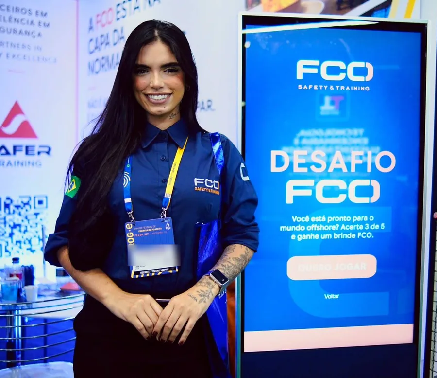 Promotora de eventos sorrindo ao lado de um totem interativo em ativação de marca numa feira