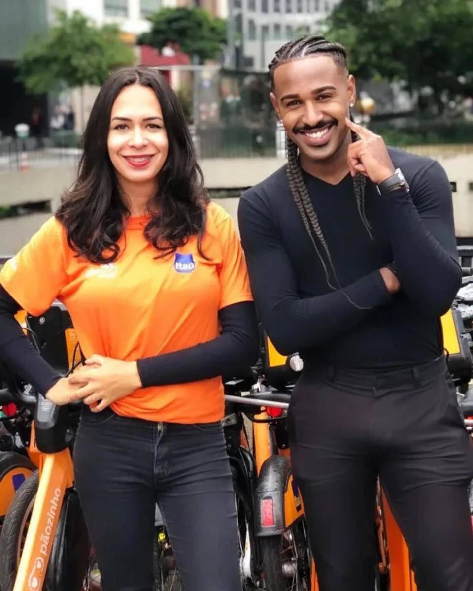 Dupla de promotores sorrindo ao lado das bicicletas laranja compartilhadas em ação de rua