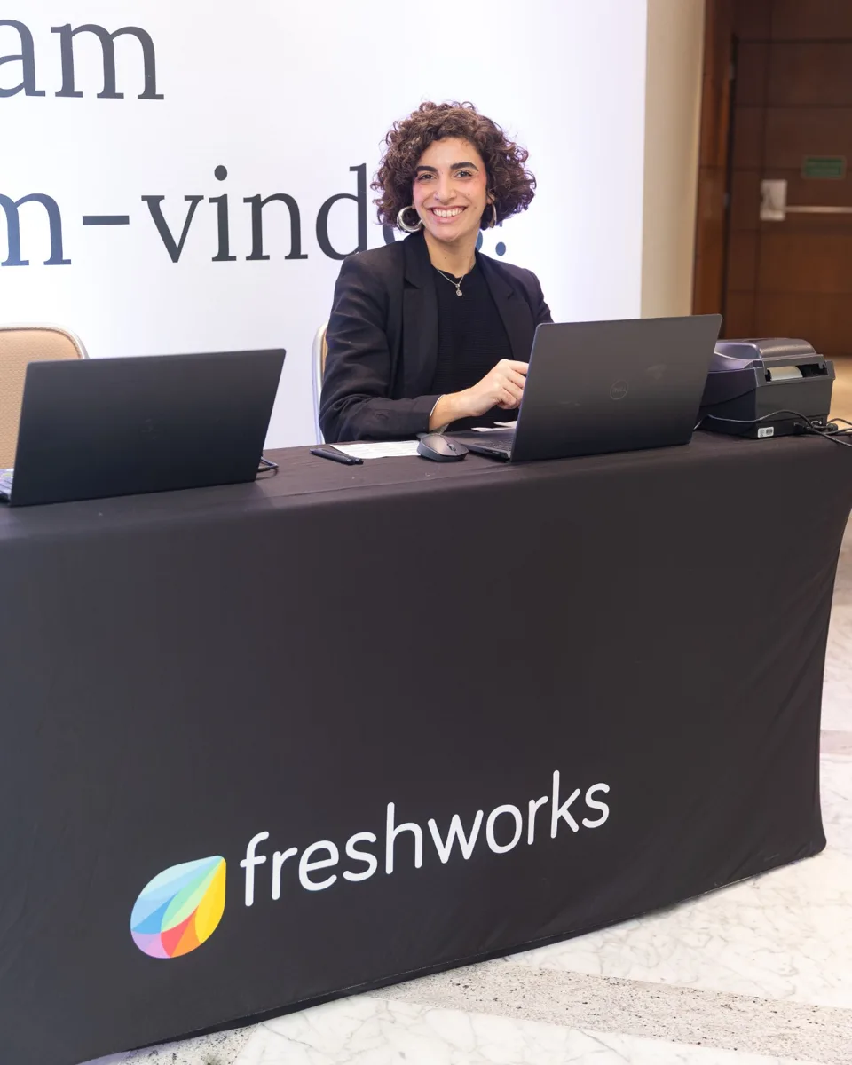 Recepcionista sorrindo no balcão de credenciamento de um summit internacional
